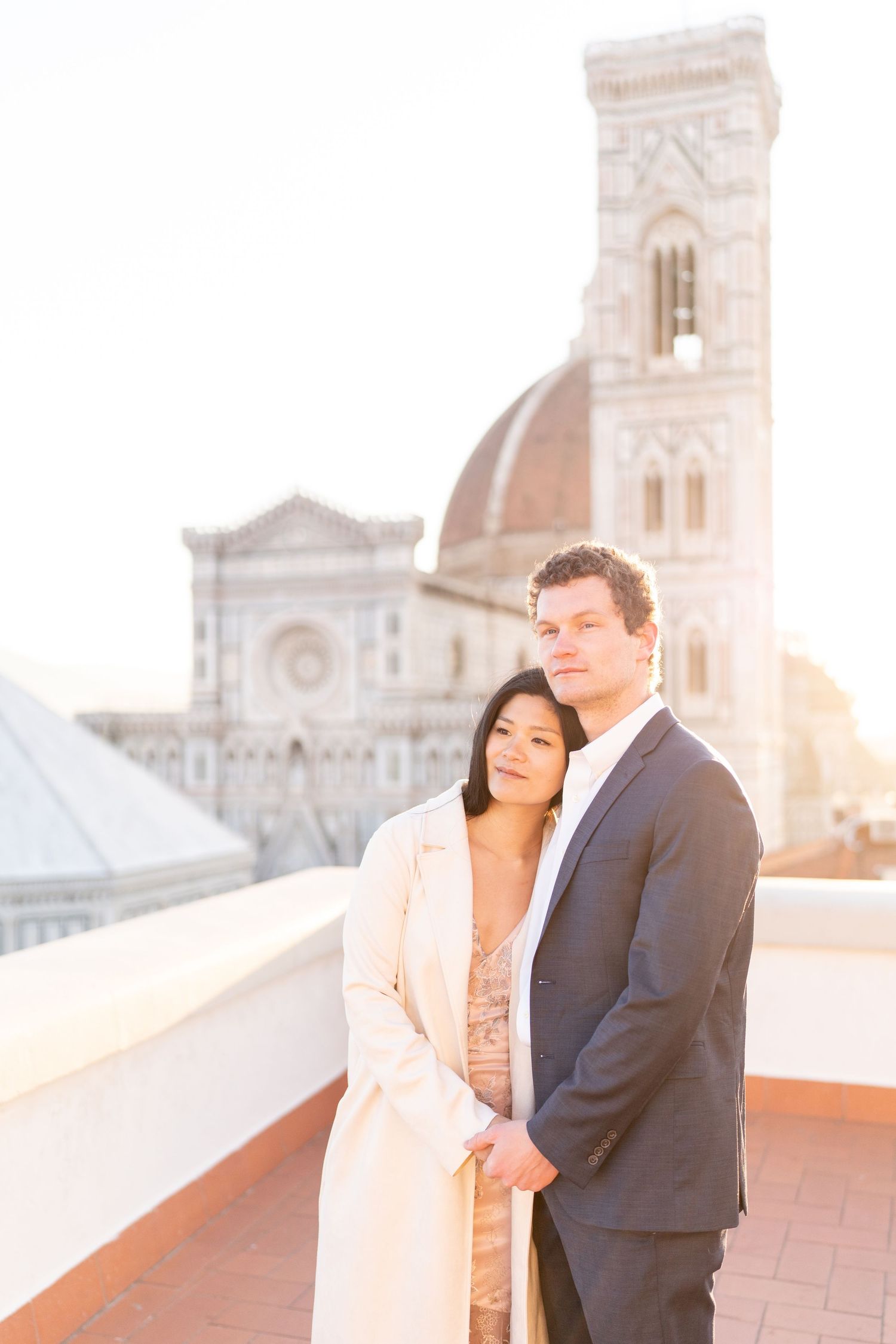 Romantic couple embraces on a rooftop terrace with a historic cathedral and sunset backdrop in Florence, Italy.