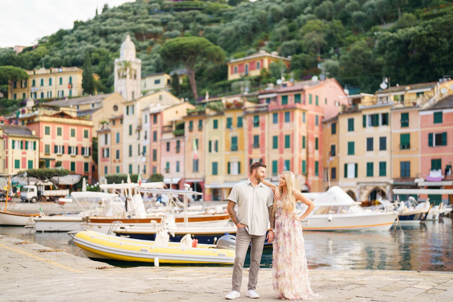A scenic panoramic view of colorful buildings and boats along the waterfront in Portofino, Italy during sunset.