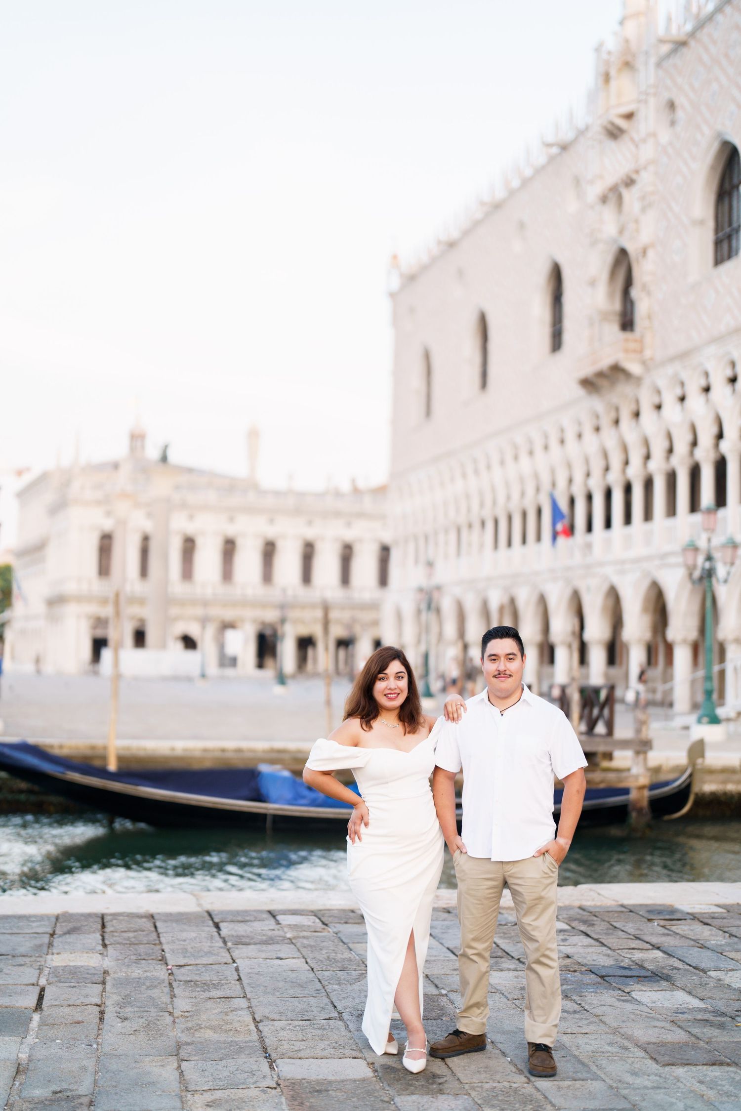Couple walking along the romantic canals and historic architecture of Venice's Doge's Palace on a sunny day.