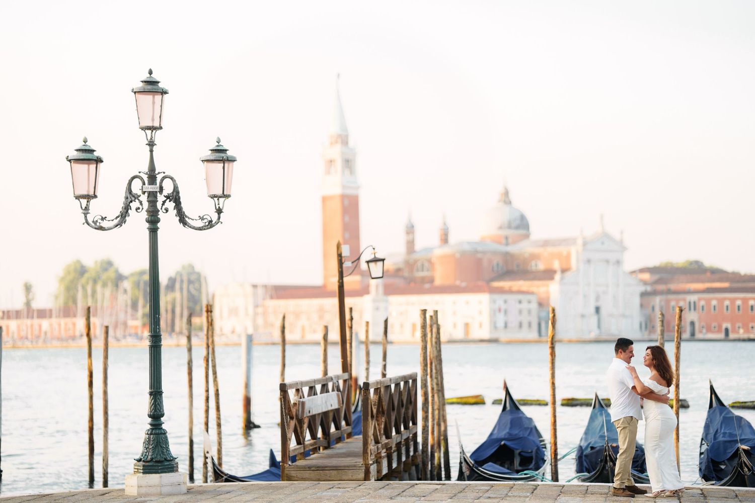 Romantic Venice cityscape with ornate lamp post, moored gondolas, and San Giorgio Maggiore church in golden sunlight.