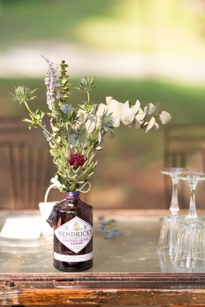 Repurposed gin bottles used as flower vases on wooden tables with elegant glassware.