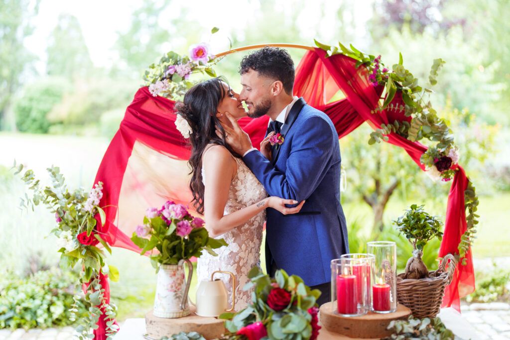 Wedding ceremony setup with red floral arch and romantic outdoor backdrop.