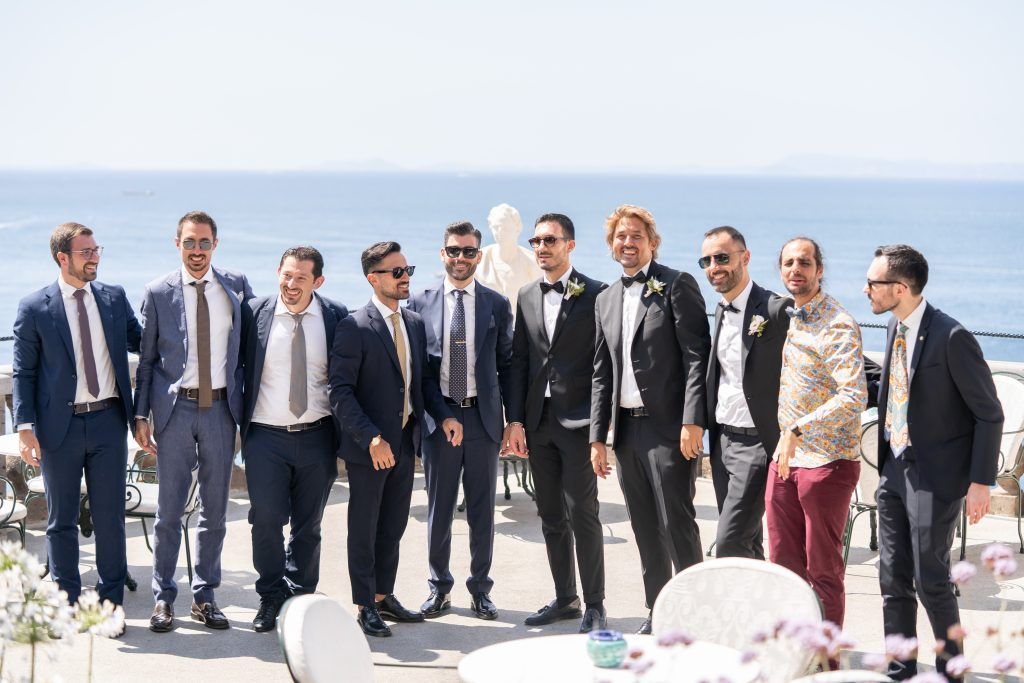 Wedding party gathered on scenic coastal terrace for group photos.