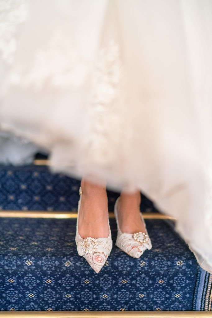 Close-up of delicate lace bridal shoes on blue patterned carpet.