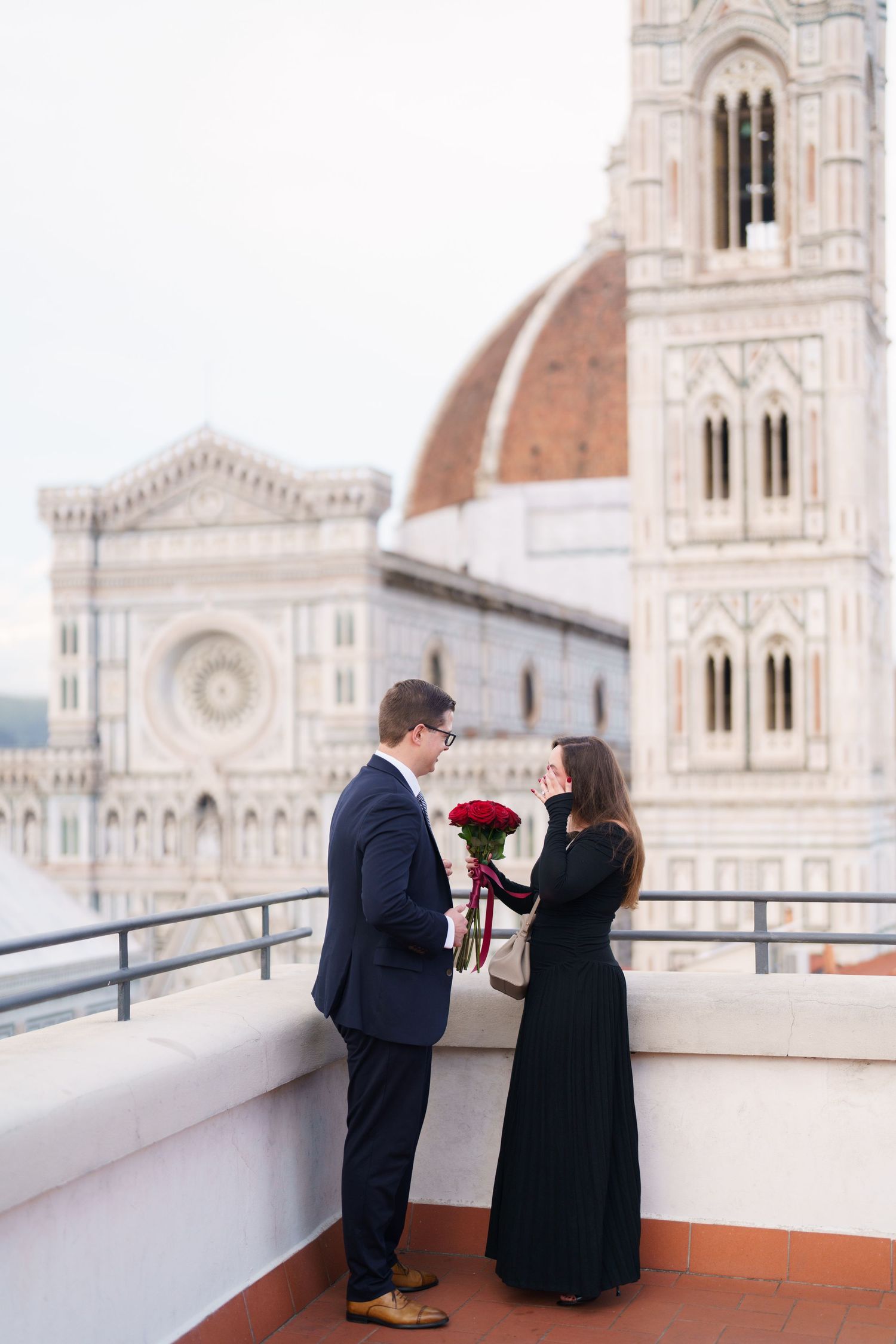 A couple shares a romantic moment on a terrace overlooking Florence Cathedral's iconic dome and architecture.