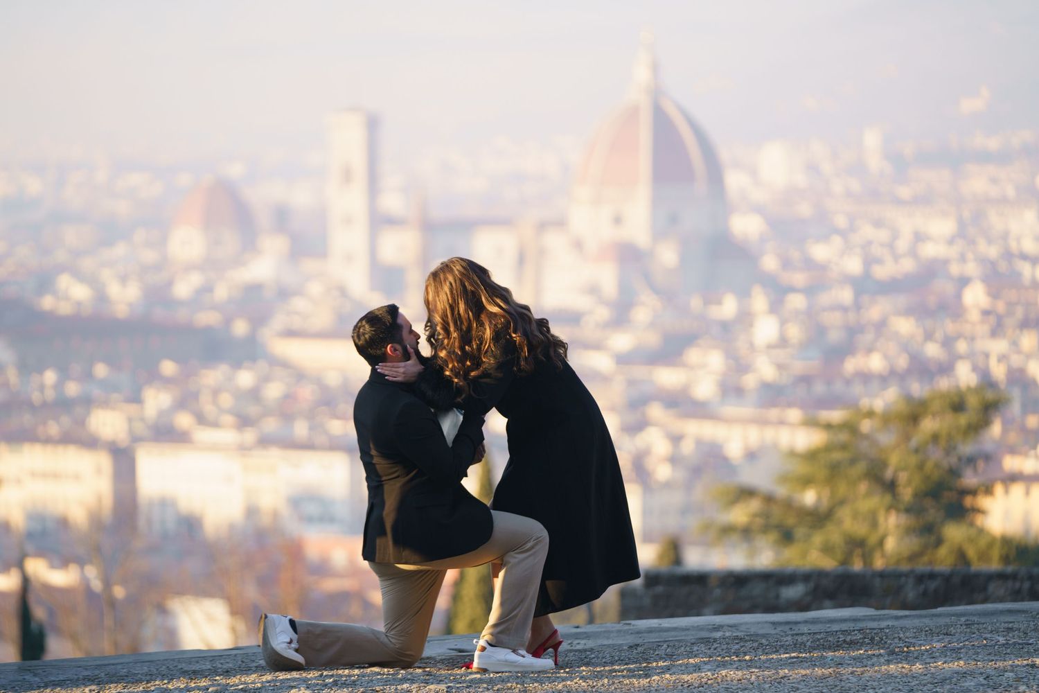 A romantic proposal moment overlooking Florence, Italy with the iconic Duomo cathedral visible in the misty cityscape below.