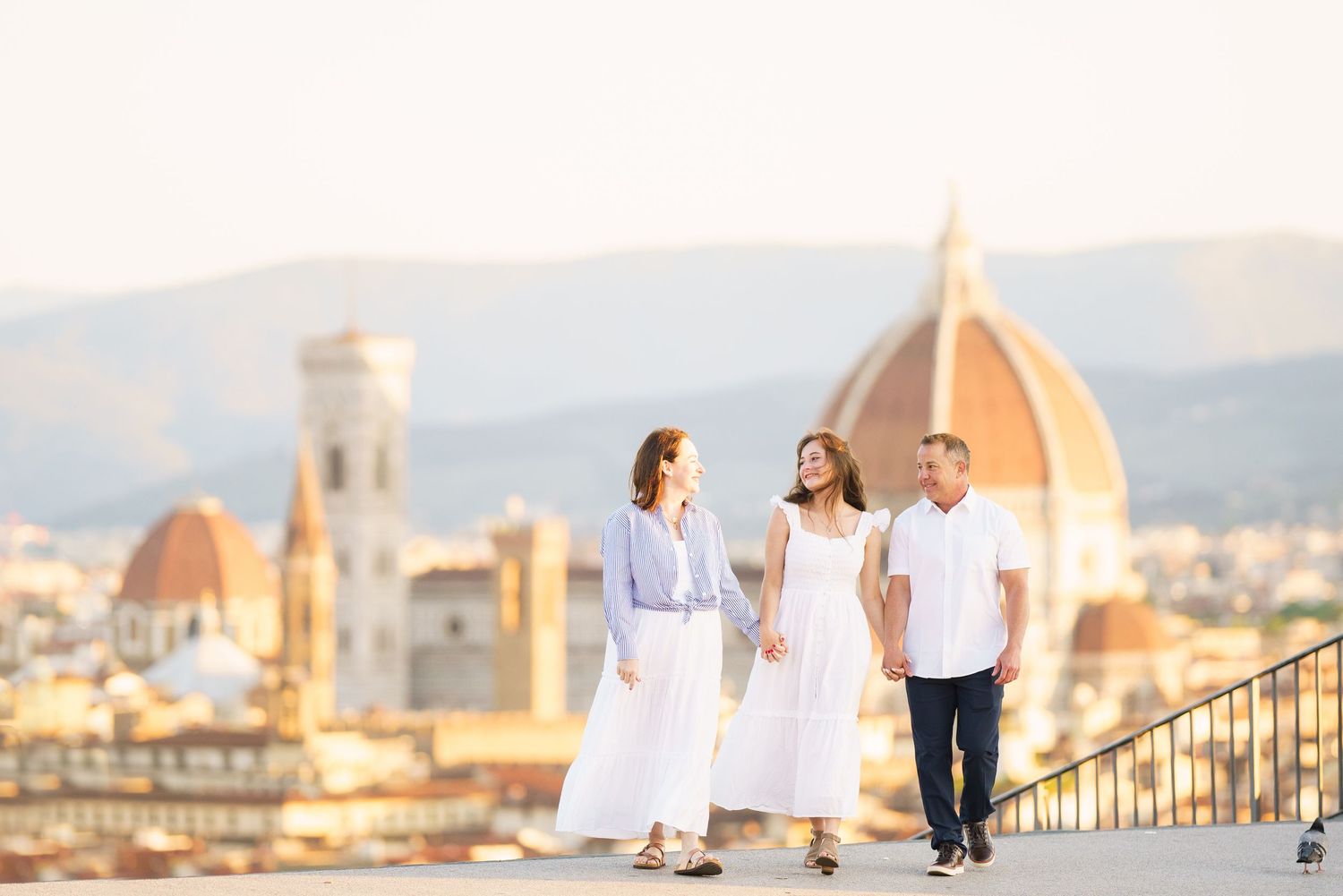 Family of three walking on a terrace with Florence cathedral dome and cityscape in golden hour light.