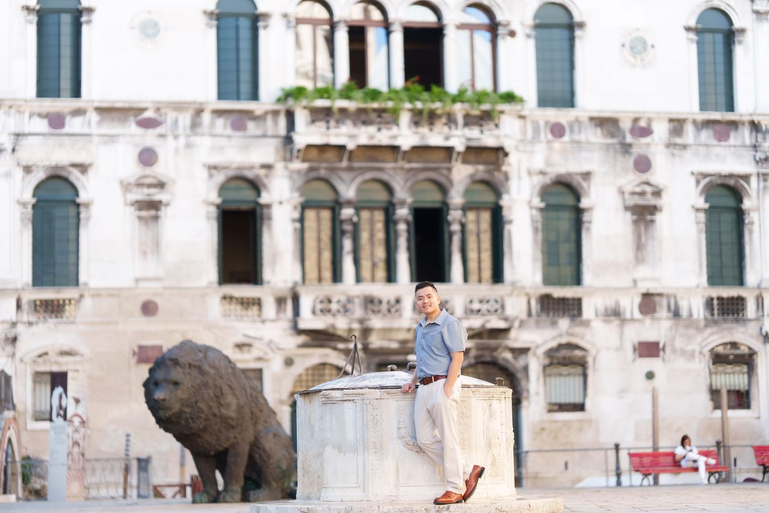 Man in casual blue shirt poses beside bronze lion sculpture in historic Venice square.