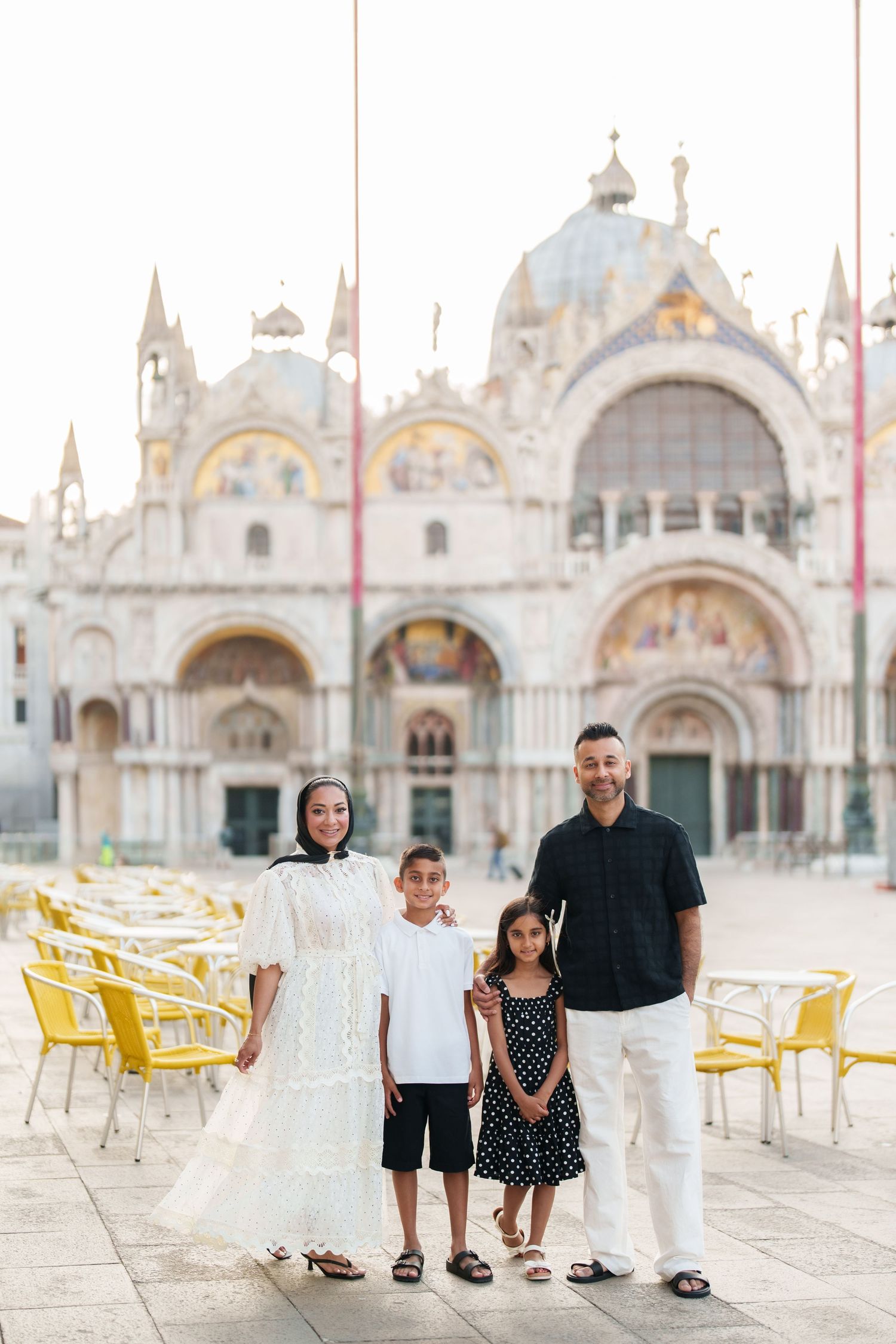 Family of four posing in front of St. Mark's Basilica in Venice, Italy on a sunny day.