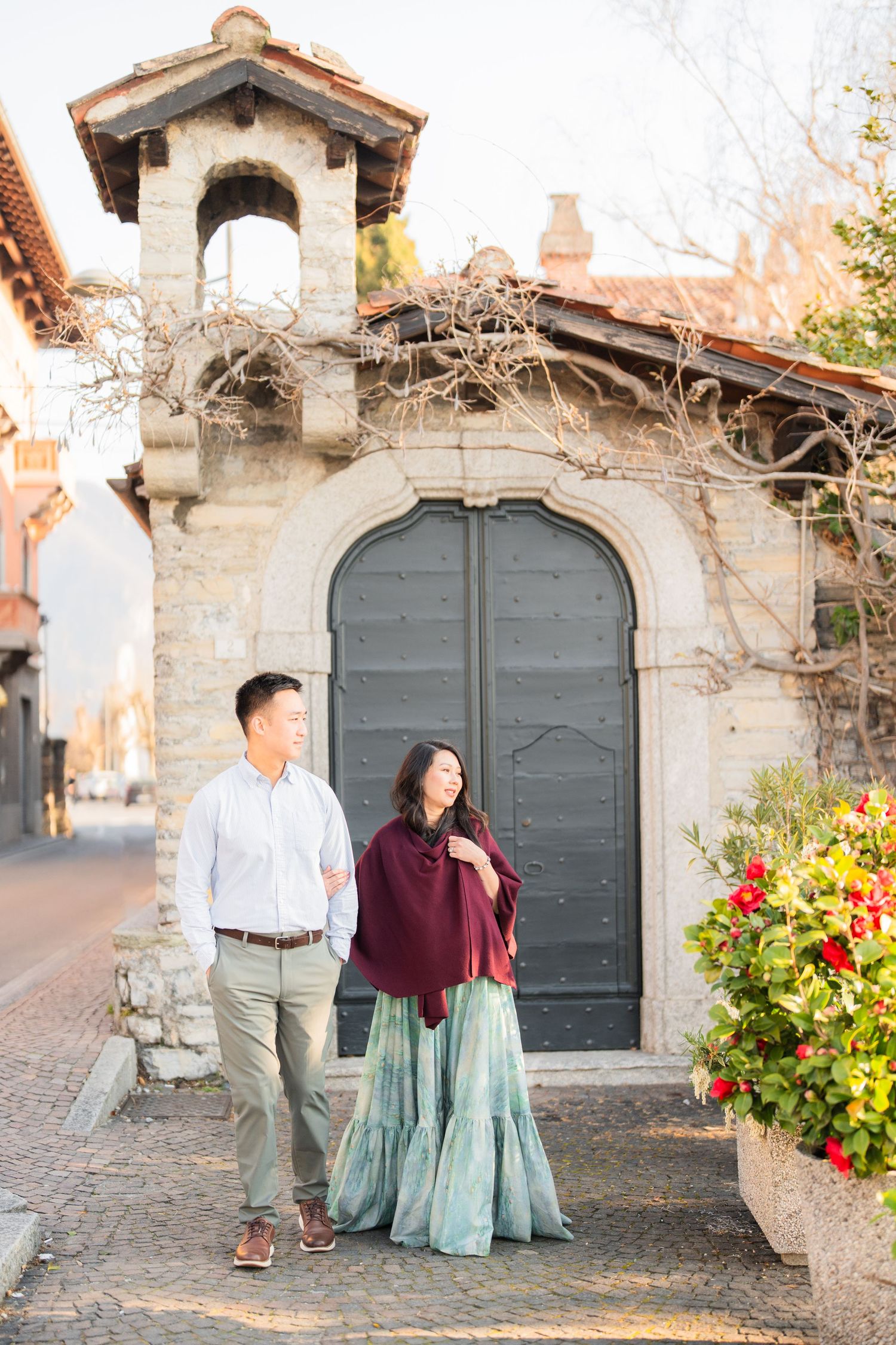 Couple walking hand in hand near a stone archway door, woman in teal skirt and burgundy wrap, man in white shirt.