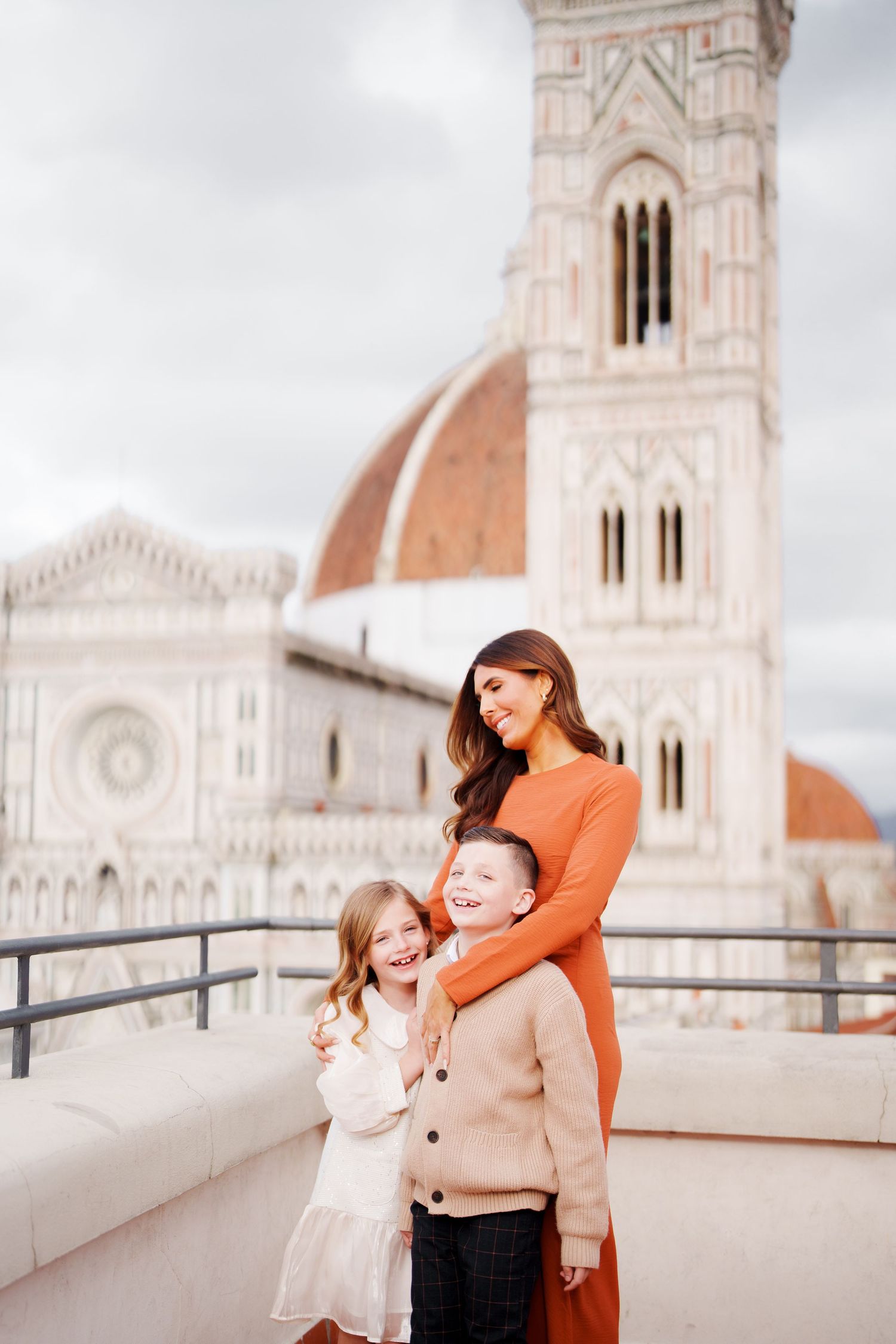 A mother and two children smile together on a rooftop terrace with Florence Cathedral's iconic dome in the background.
