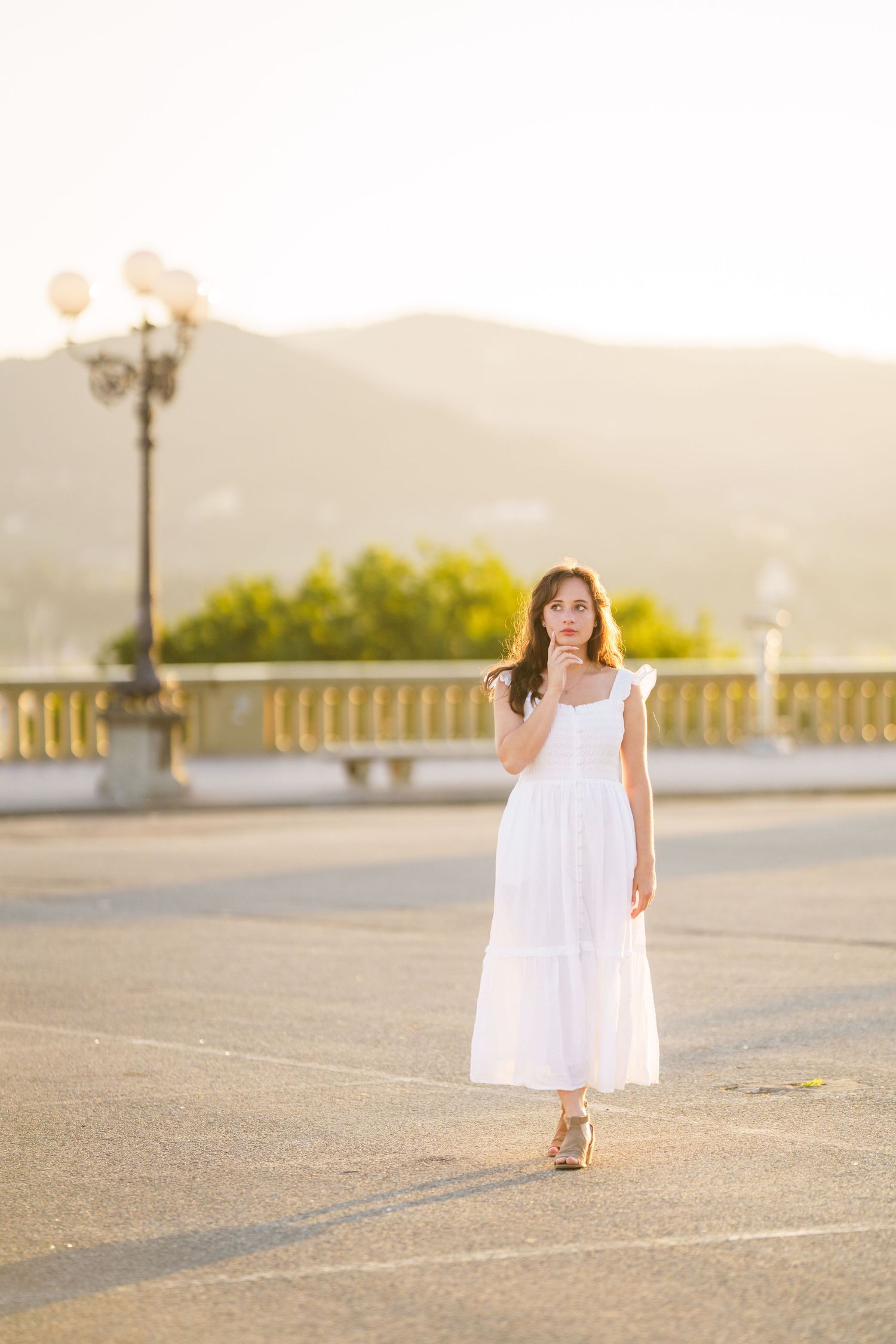 A young girl in a white dress walks across a sun-lit concrete plaza during golden hour.