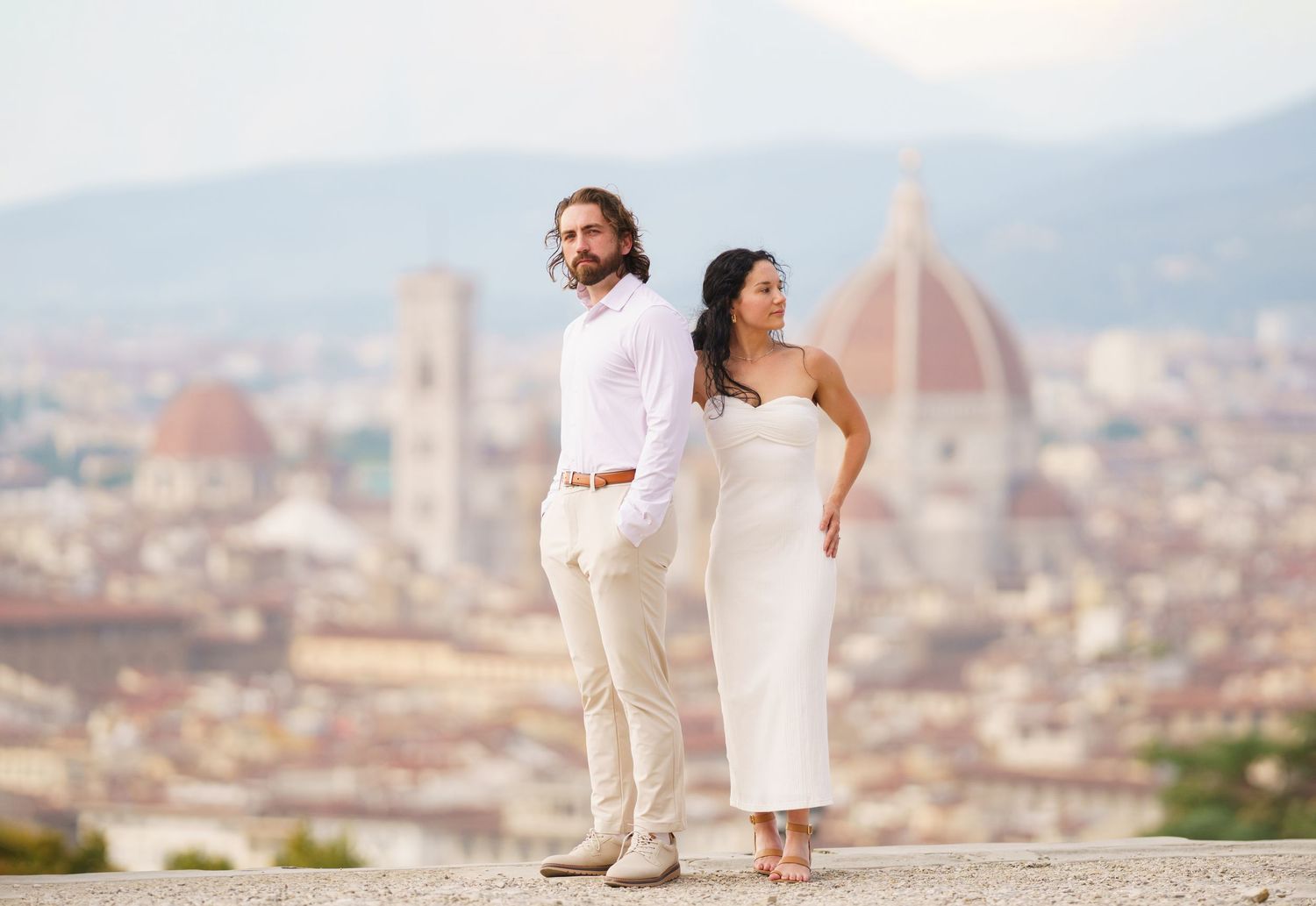 A couple poses together on a scenic overlook with Florence's iconic Duomo cathedral and cityscape in the background.