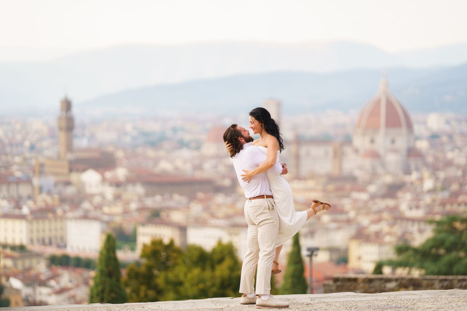 A couple shares a romantic moment overlooking the historic skyline of Florence, Italy from Piazzale Michelangelo.