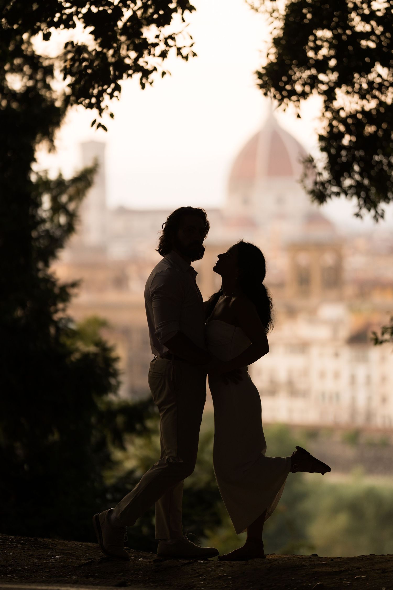 A romantic silhouette of a couple embracing against a sunset cityscape with Florence's Duomo cathedral in the background.