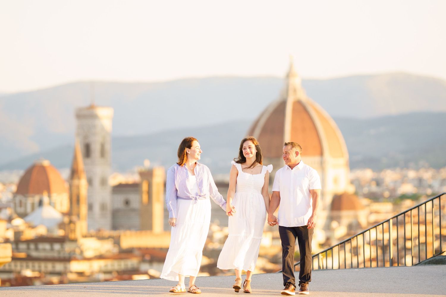 People in white outfits pose for photos with Florence's iconic Duomo cathedral and cityscape in the golden sunset light.