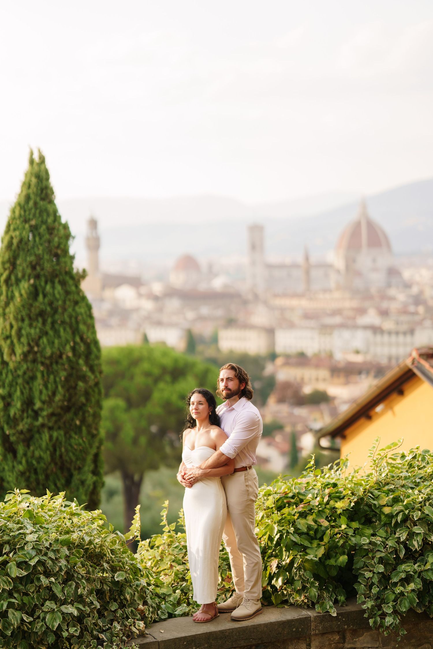 A couple sits together overlooking the historic skyline of Florence, Italy from a scenic hilltop garden viewpoint.