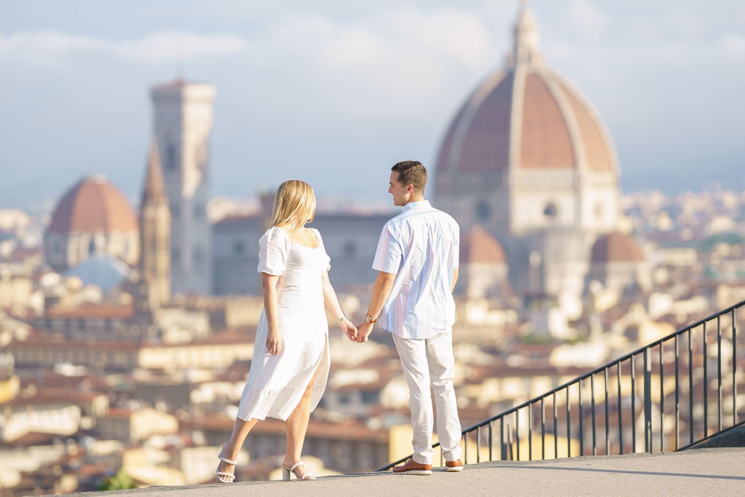 Couple in white clothing walking up stone steps overlooking the iconic Florence skyline with Duomo cathedral in Italy.