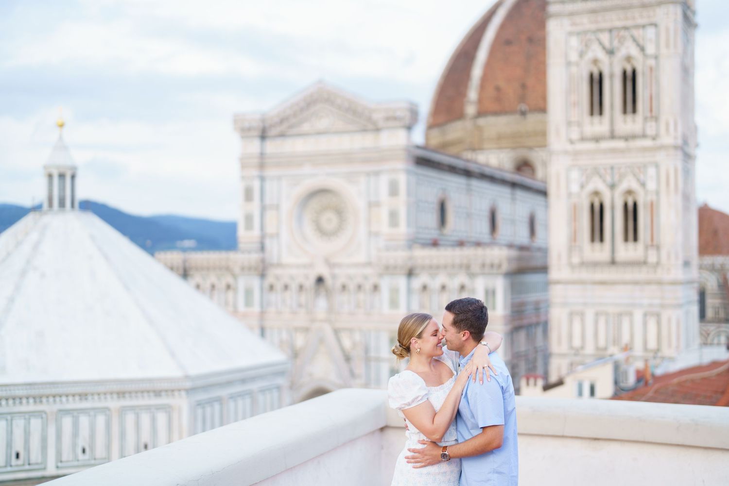 A couple in formal wedding attire poses on a terrace overlooking the Florence Cathedral and Duomo in Italy.