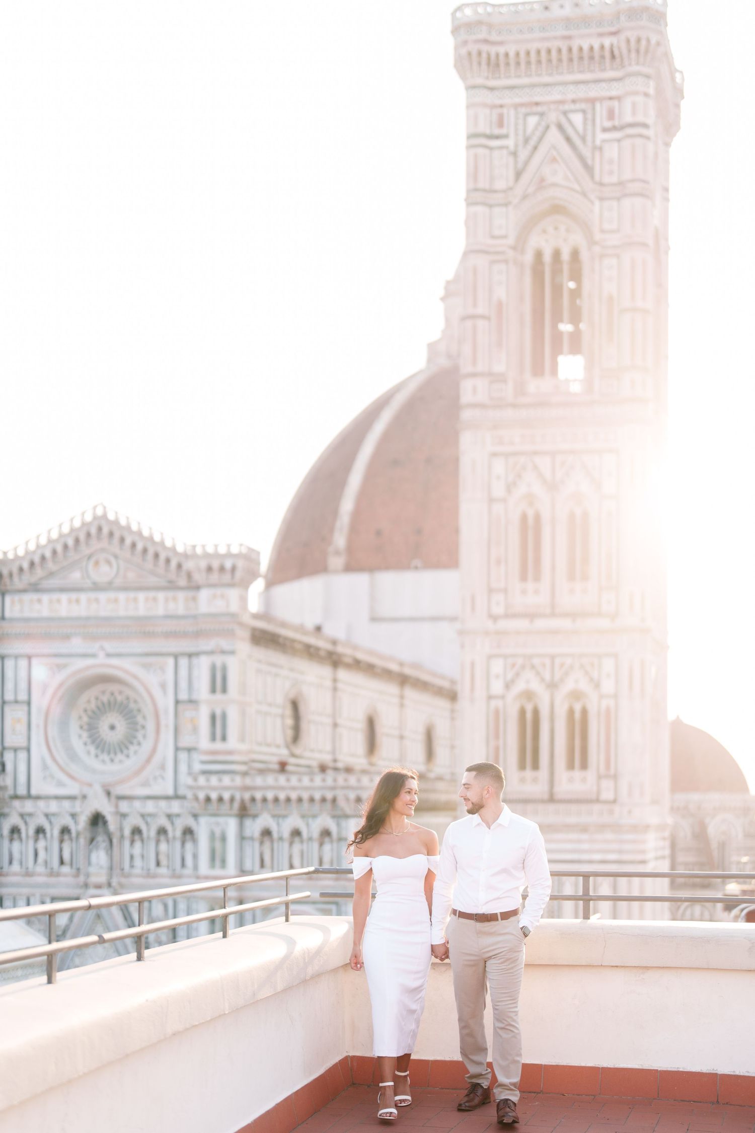 A romantic couple shares a tender moment on a rooftop terrace overlooking the Duomo cathedral in Florence, Italy at sunset.