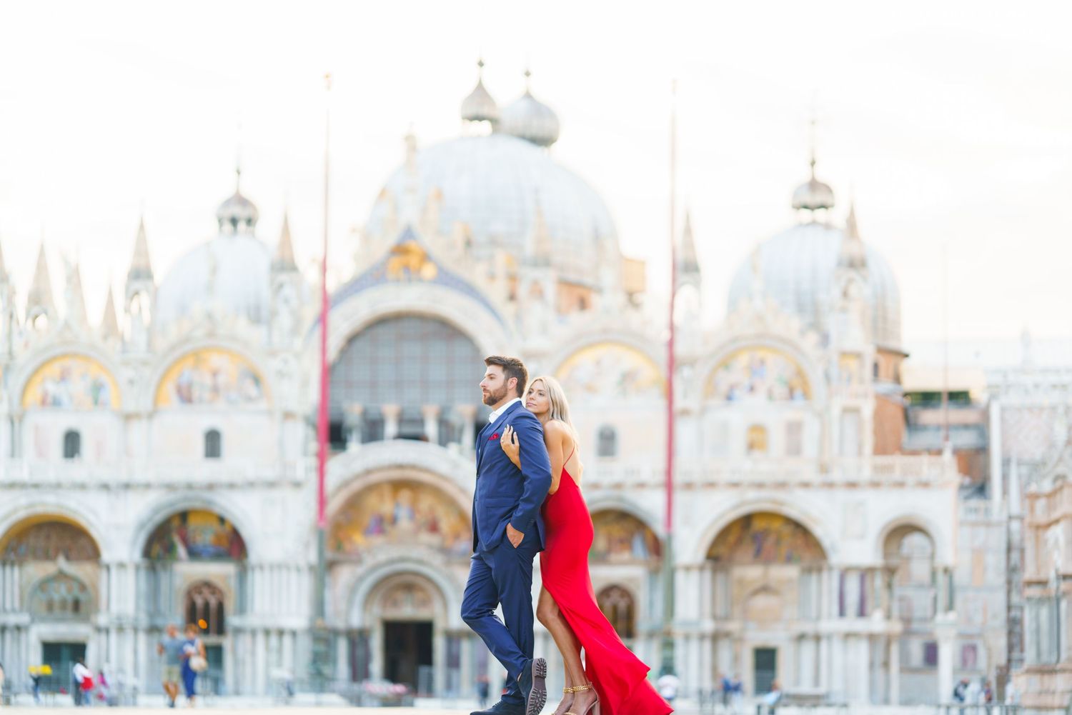 A couple in formal attire poses in front of St. Mark's Basilica in Venice, Italy with flowing red fabric.