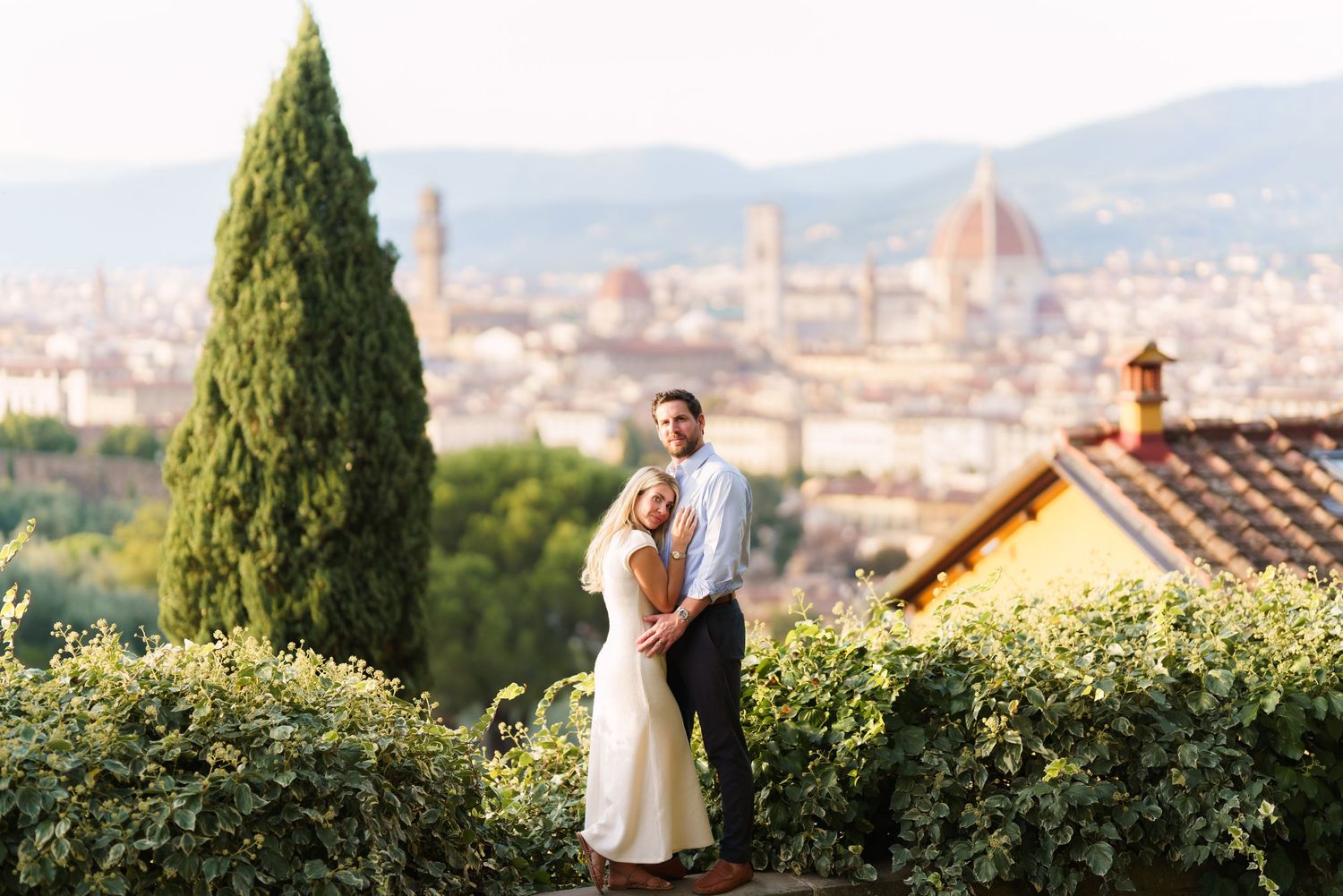 A couple shares a romantic moment overlooking the scenic Florence cityscape from a hilltop garden terrace.