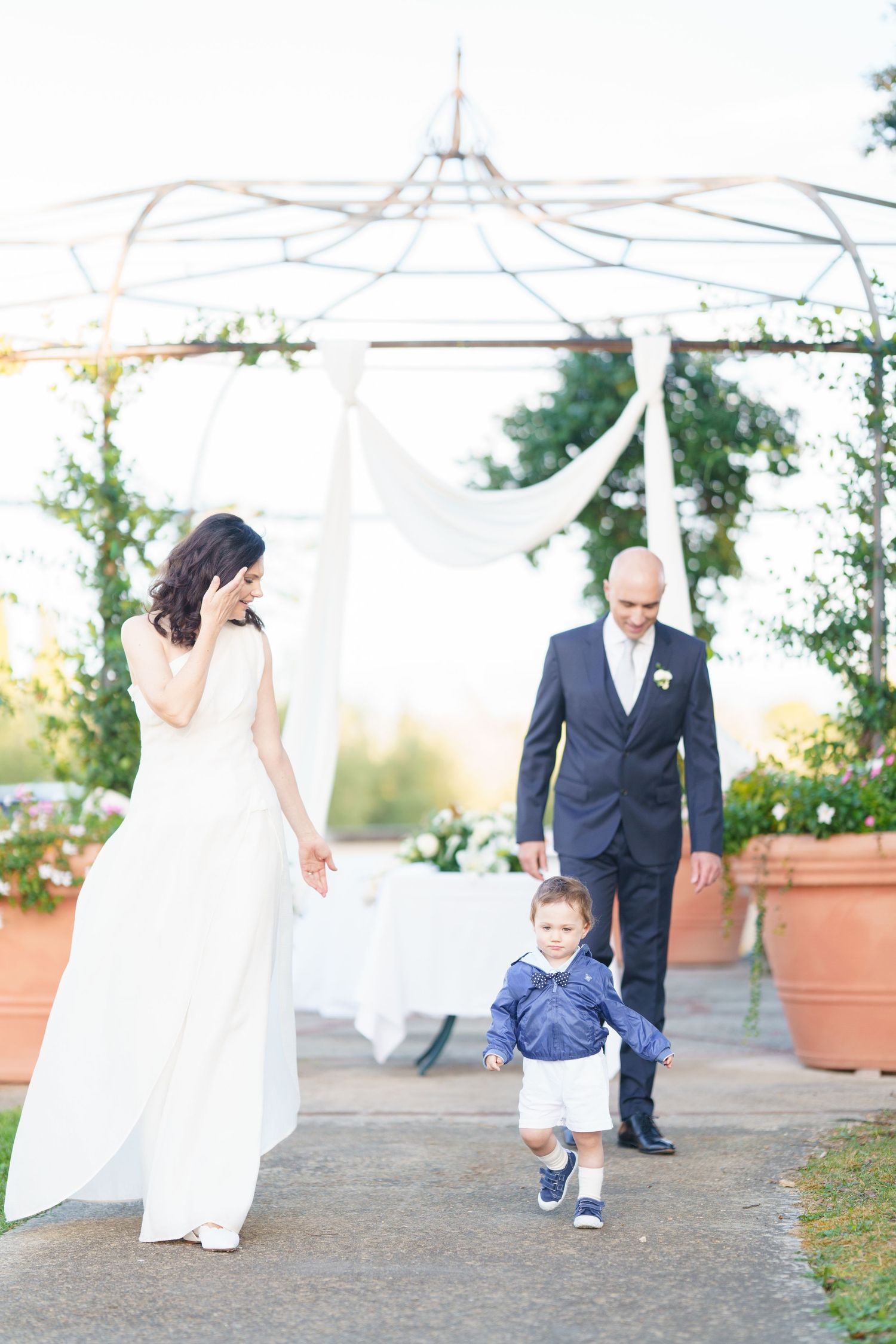 Candid wedding moments captured under white canopy with terra cotta planters in garden setting.