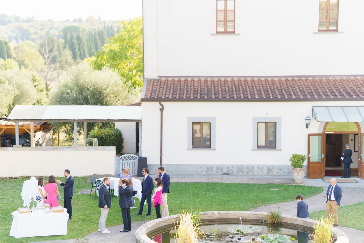 Outdoor wedding ceremony setup with guests gathering near a white building.