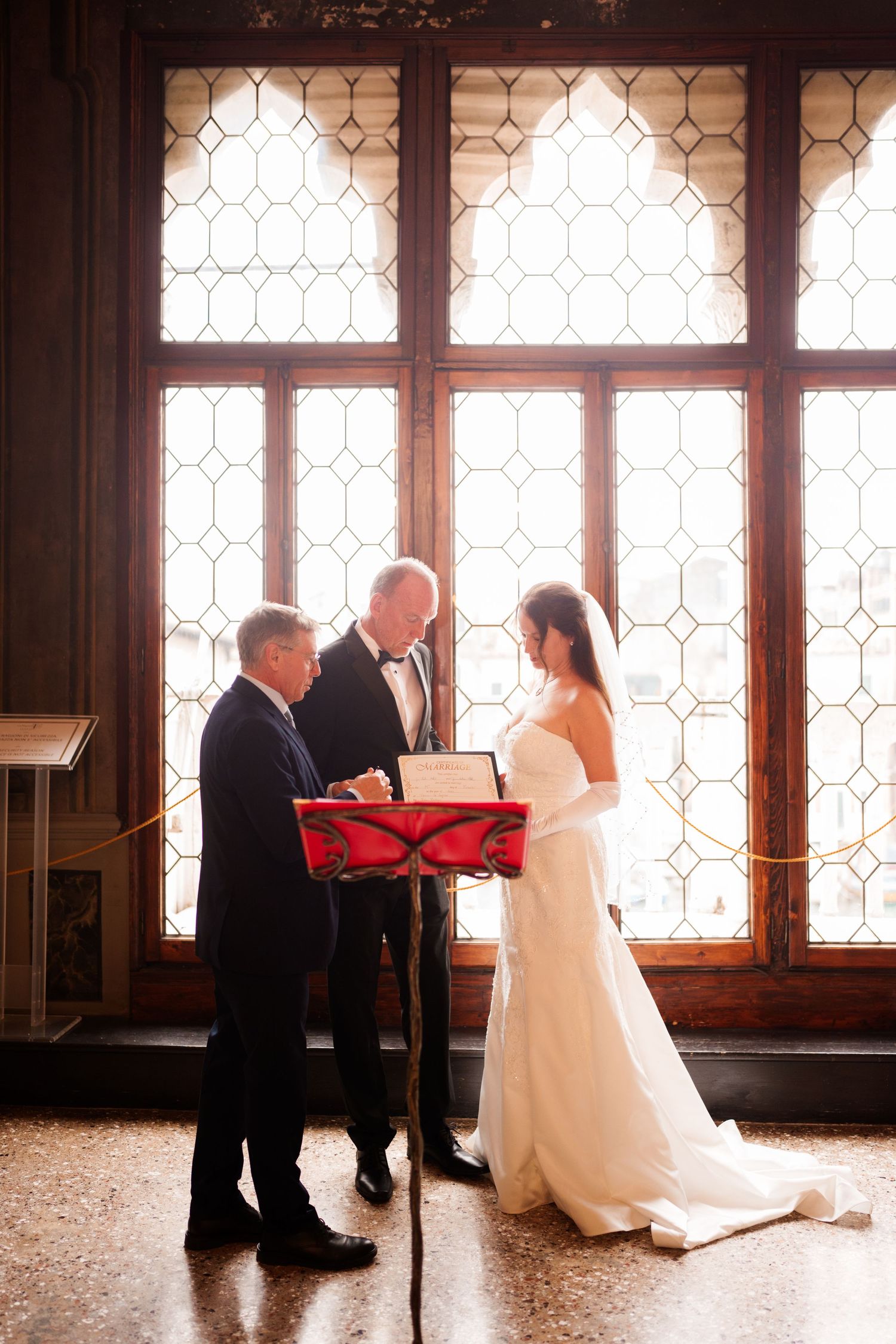 A wedding ceremony sequence showing a couple exchanging vows in front of ornate windows in a historic venue.