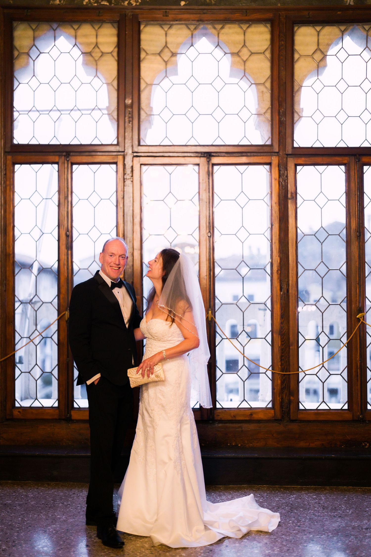 Romantic wedding couple dances in front of elegant leaded glass windows in a historic venue.