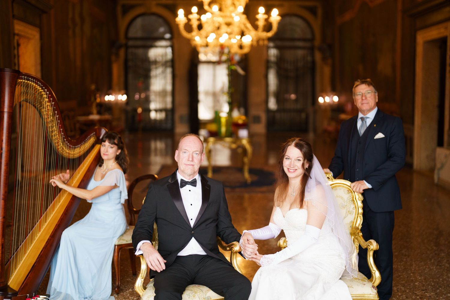 A wedding party dances and celebrates in an elegant ballroom with crystal chandeliers and golden decor.