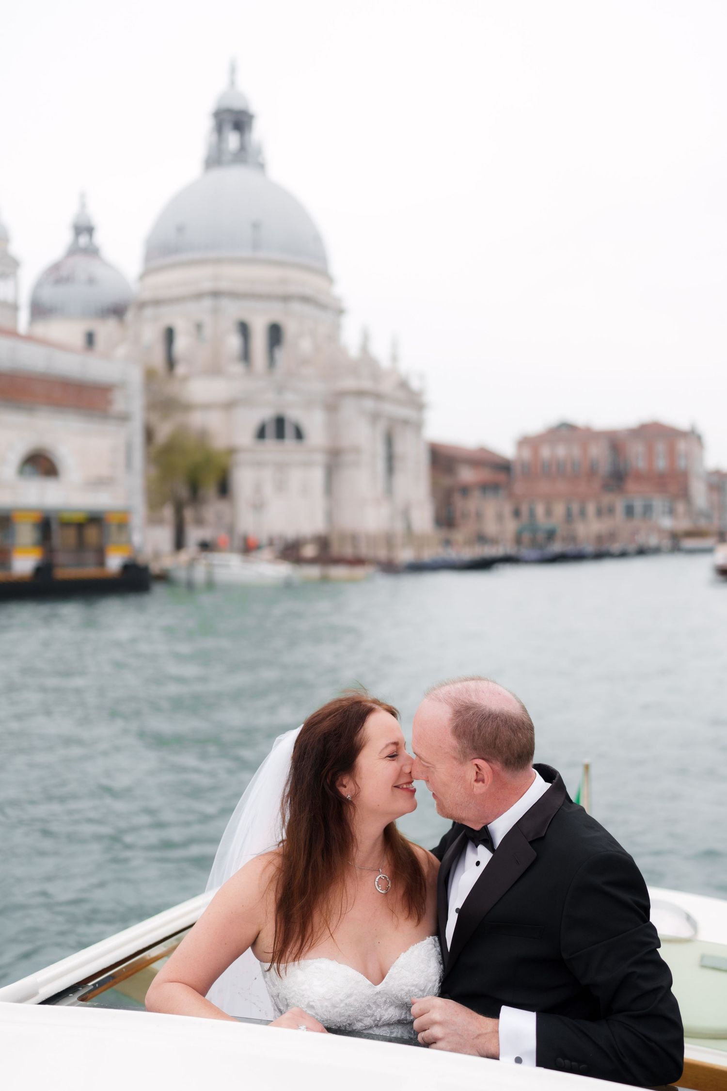 A couple shares a romantic moment on a boat in Venice with the iconic Santa Maria della Salute church in the background.