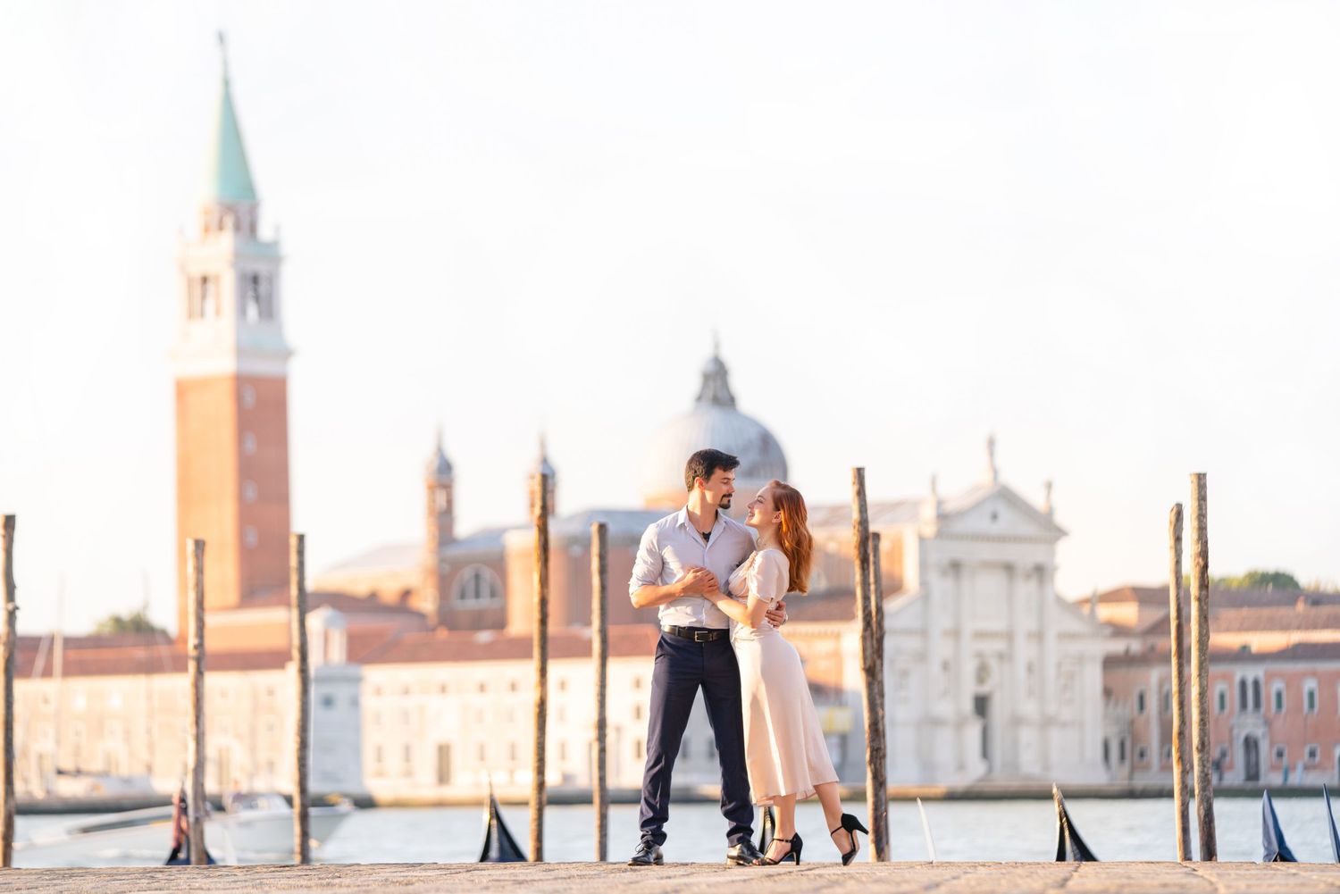 A couple shares a romantic moment in Venice with the iconic San Giorgio Maggiore church and bell tower in the background.