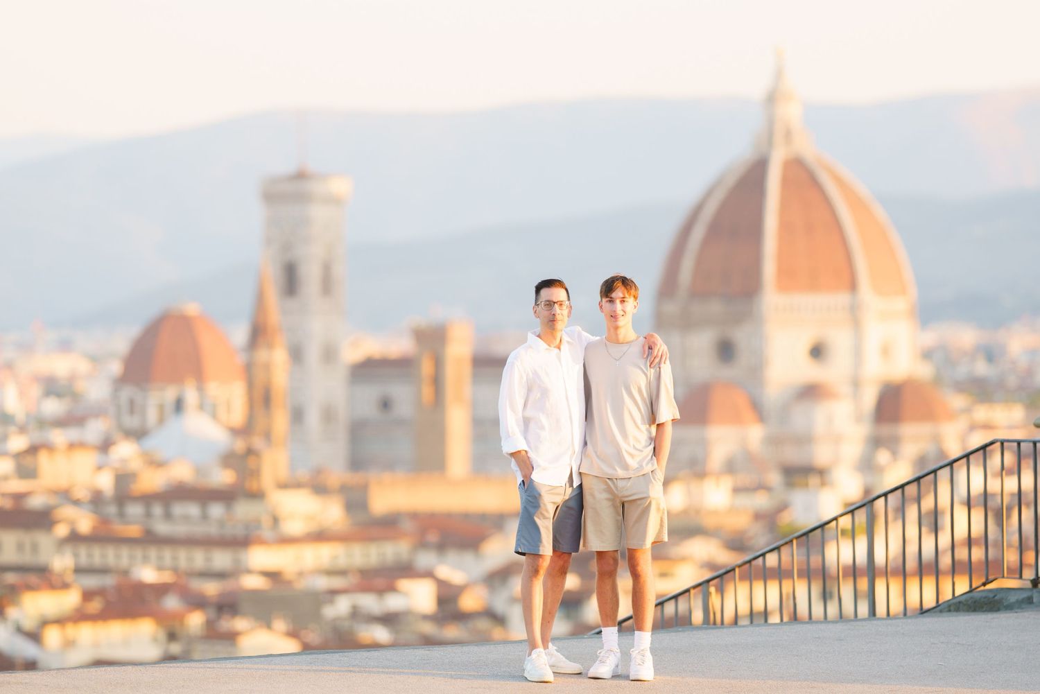 Couple walking along a scenic bridge overlooking Florence's iconic Duomo and historic cityscape at sunset.