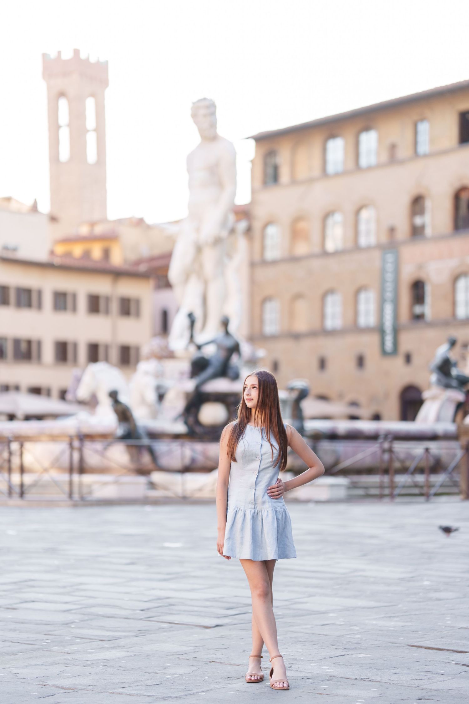 A person in a white dress poses in front of historic Italian architecture in Florence's Piazza della Signoria.