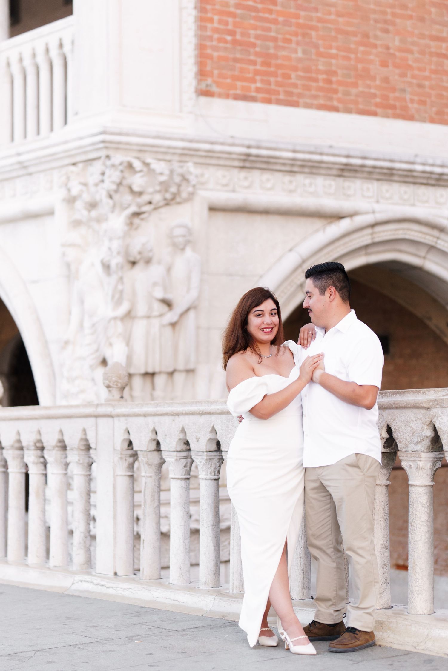 Romantic couple in white outfits sharing intimate moments along ornate stone balustrades at sunset.
