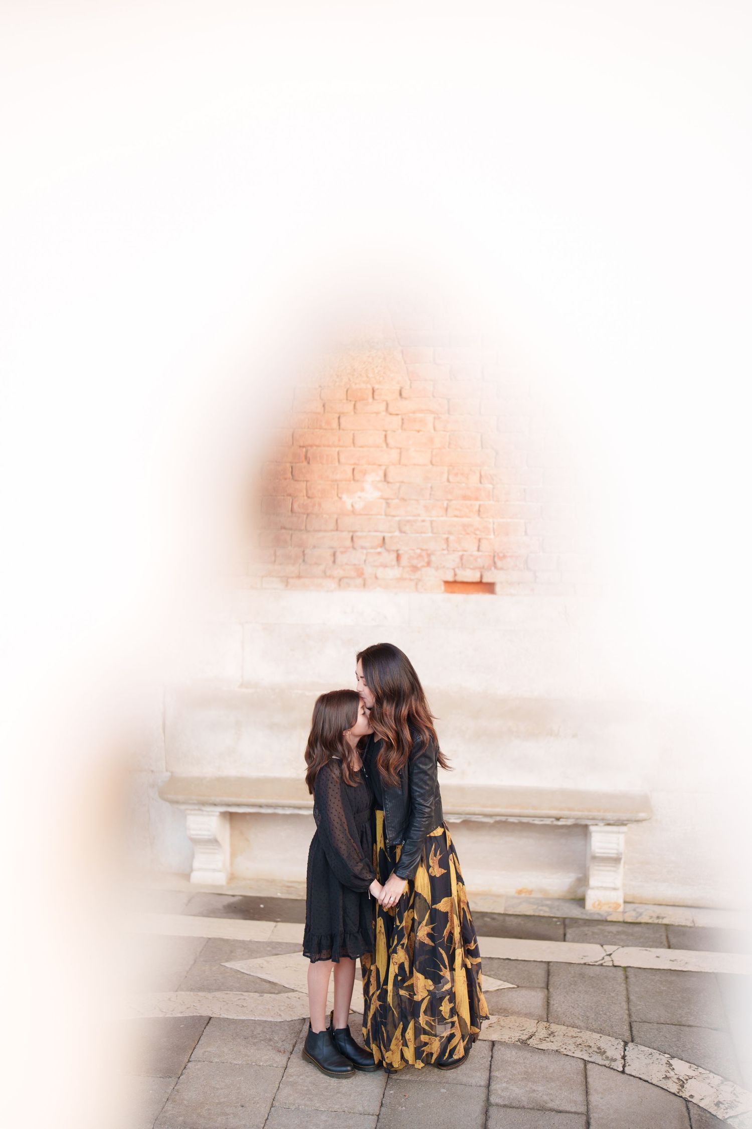 Two people sit together on stone steps in matching black outfits with a yellow patterned bag beside them.