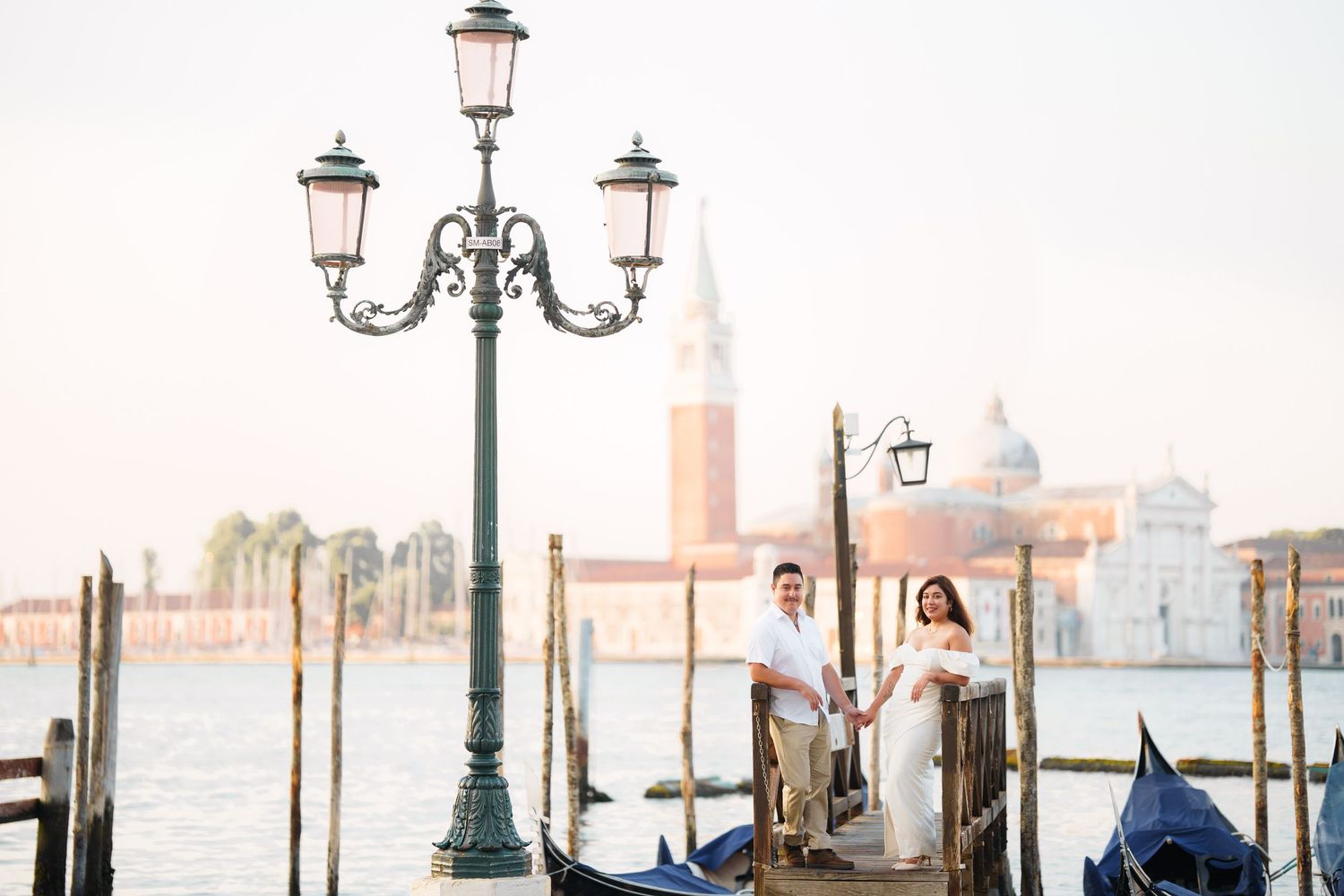 Ornate street lamp and gondolas along Venice's Grand Canal with historic buildings and church domes in the background.