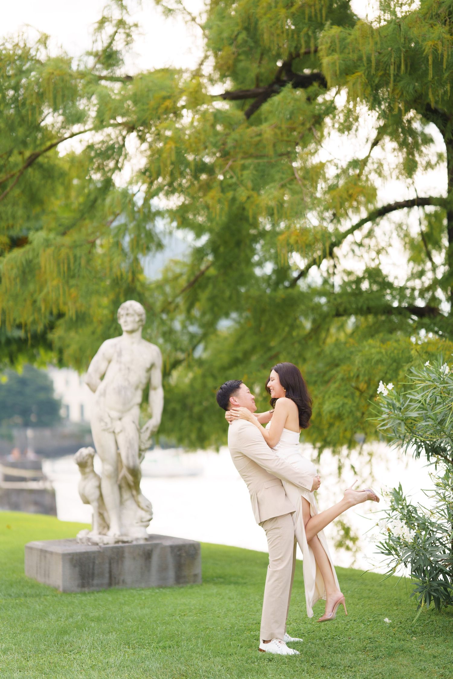 A romantic couple shares tender moments in a park with a stone statue visible in the background.