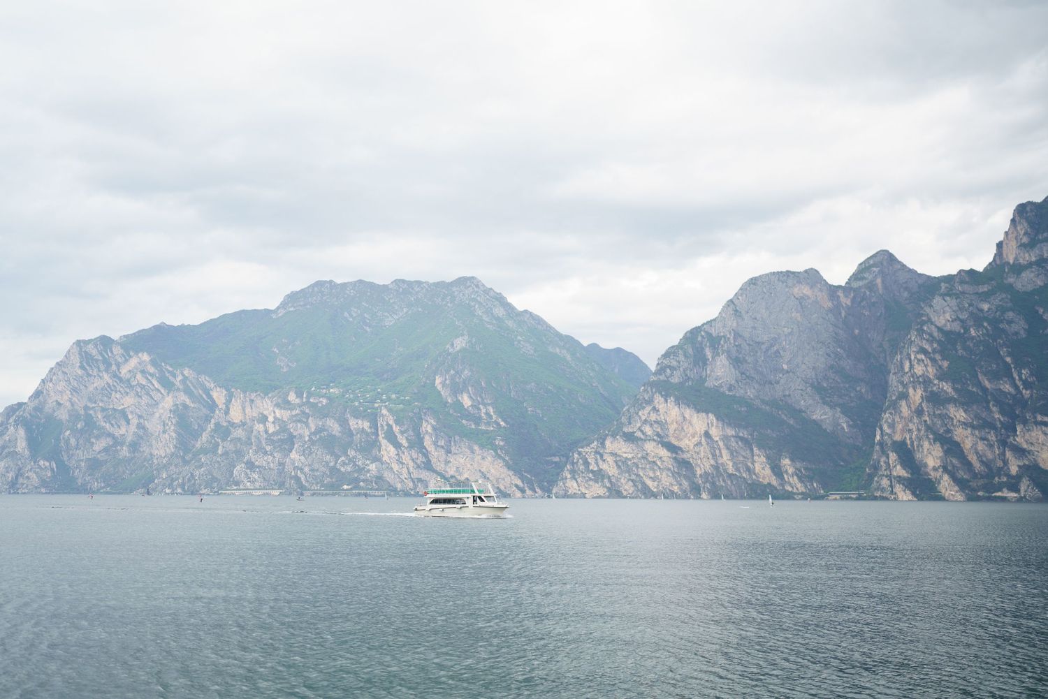 A panoramic view of rugged mountain peaks rising above a misty lake with a boat in the distance.