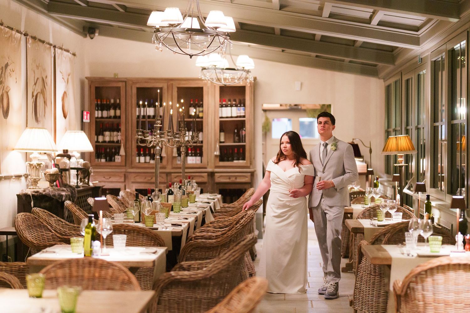 Elegant restaurant interior with wooden bar, rattan chairs and chandeliers.