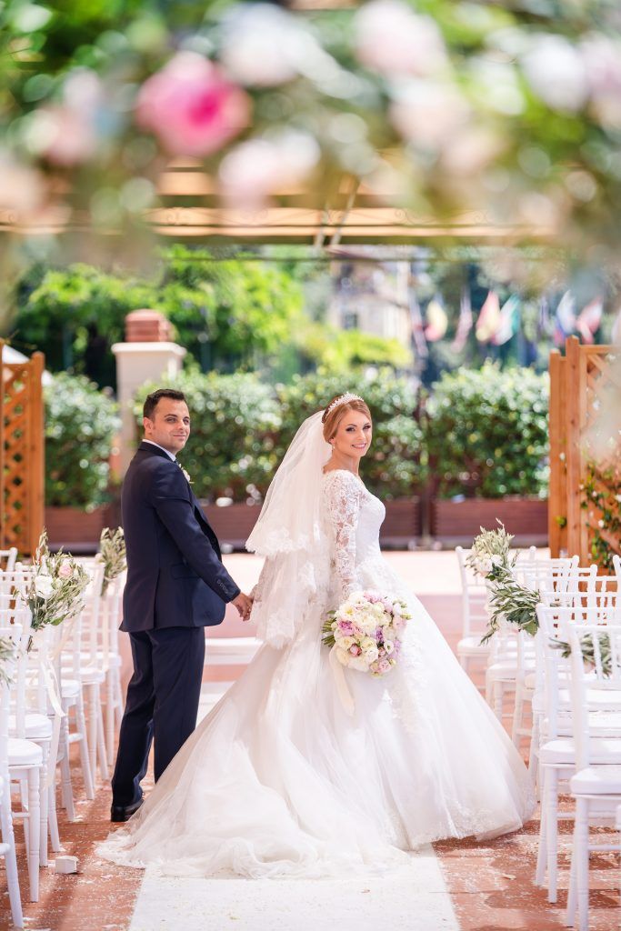Wedding ceremony setup with white chairs and floral arrangements in an outdoor garden setting.