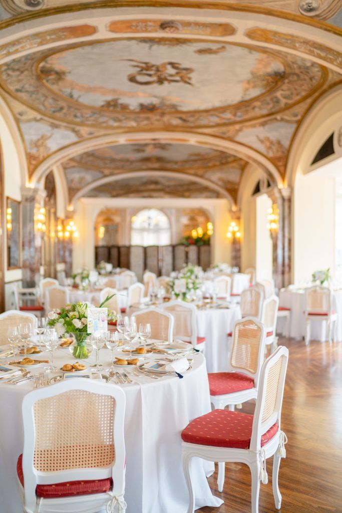 Elegant wedding reception setup with round tables in baroque-style ballroom with frescoed ceiling.