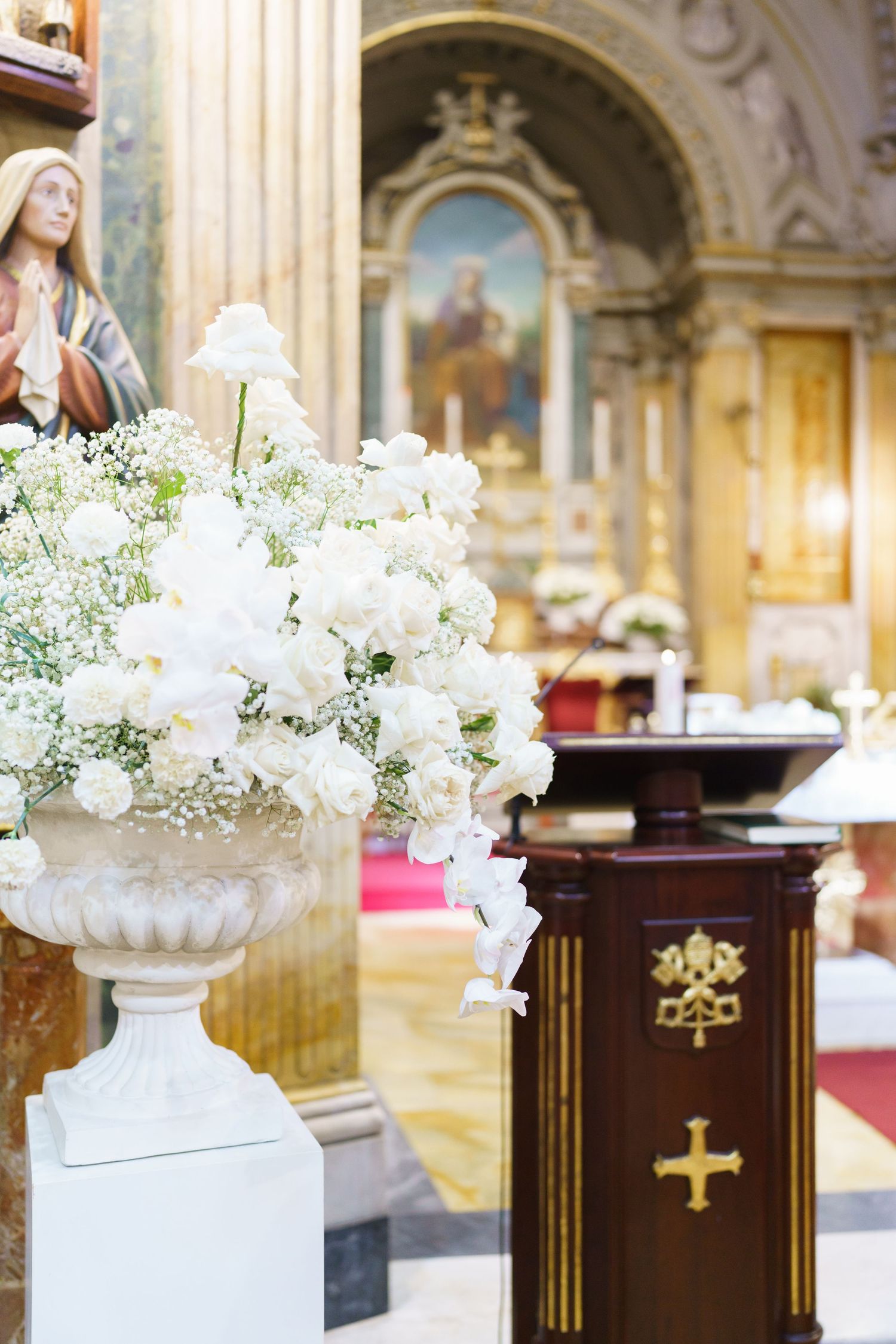 Elegant white floral arrangements in classical urns decorating church altar.