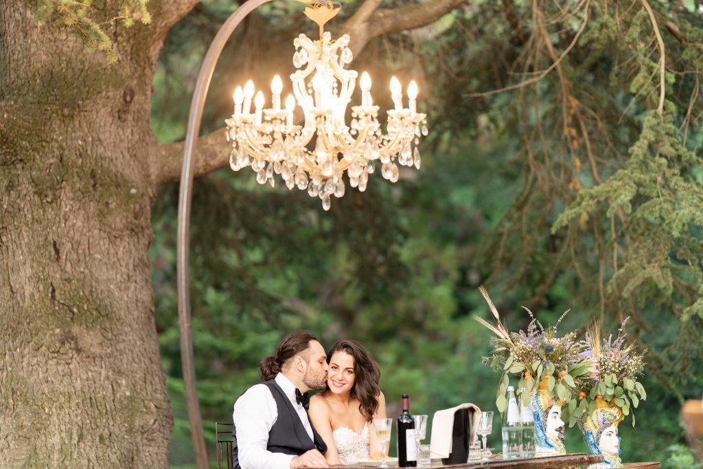 Romantic outdoor setting with illuminated crystal chandeliers hanging from tree branches.