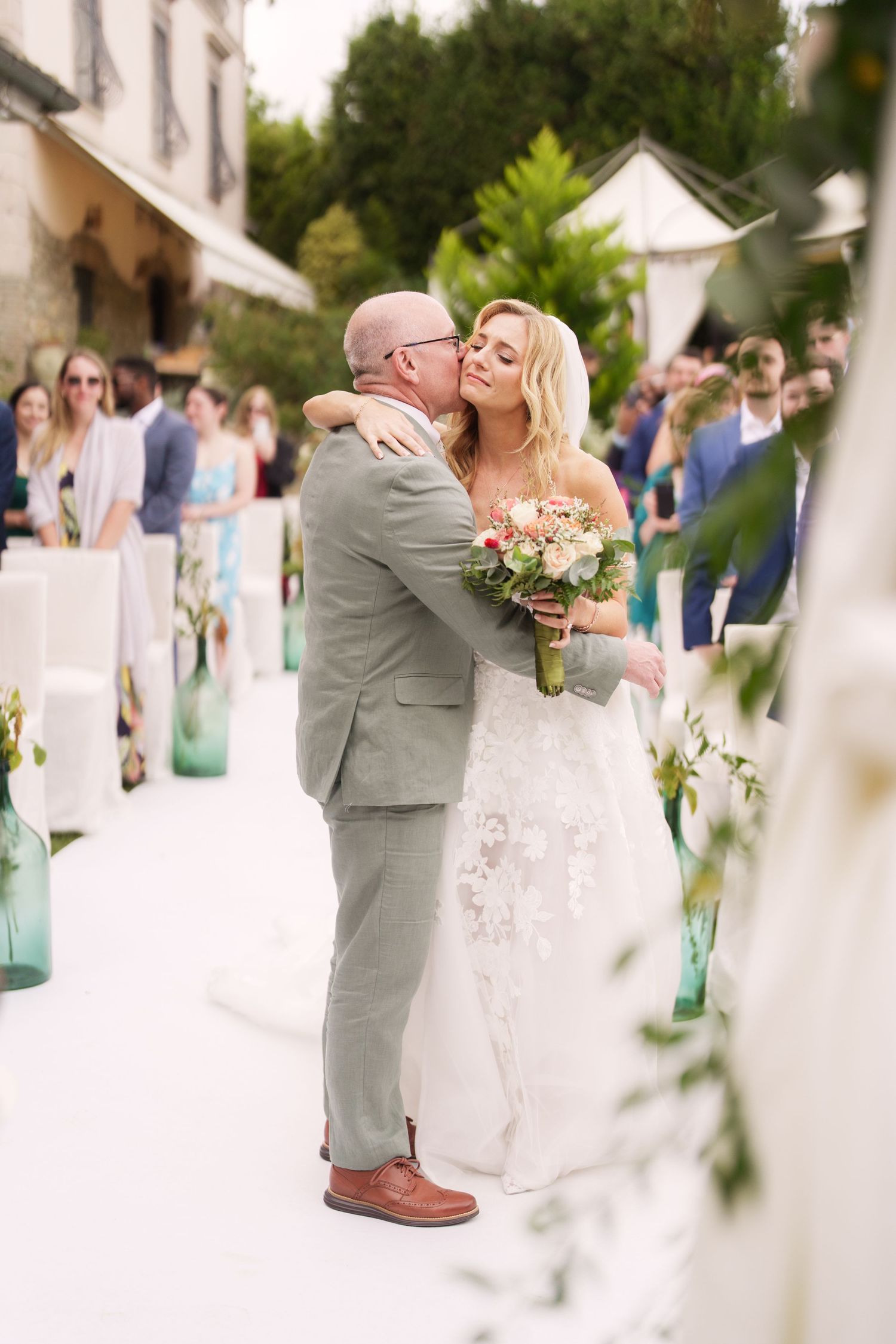 A tender moment captured during a wedding ceremony with guests looking on in the background.