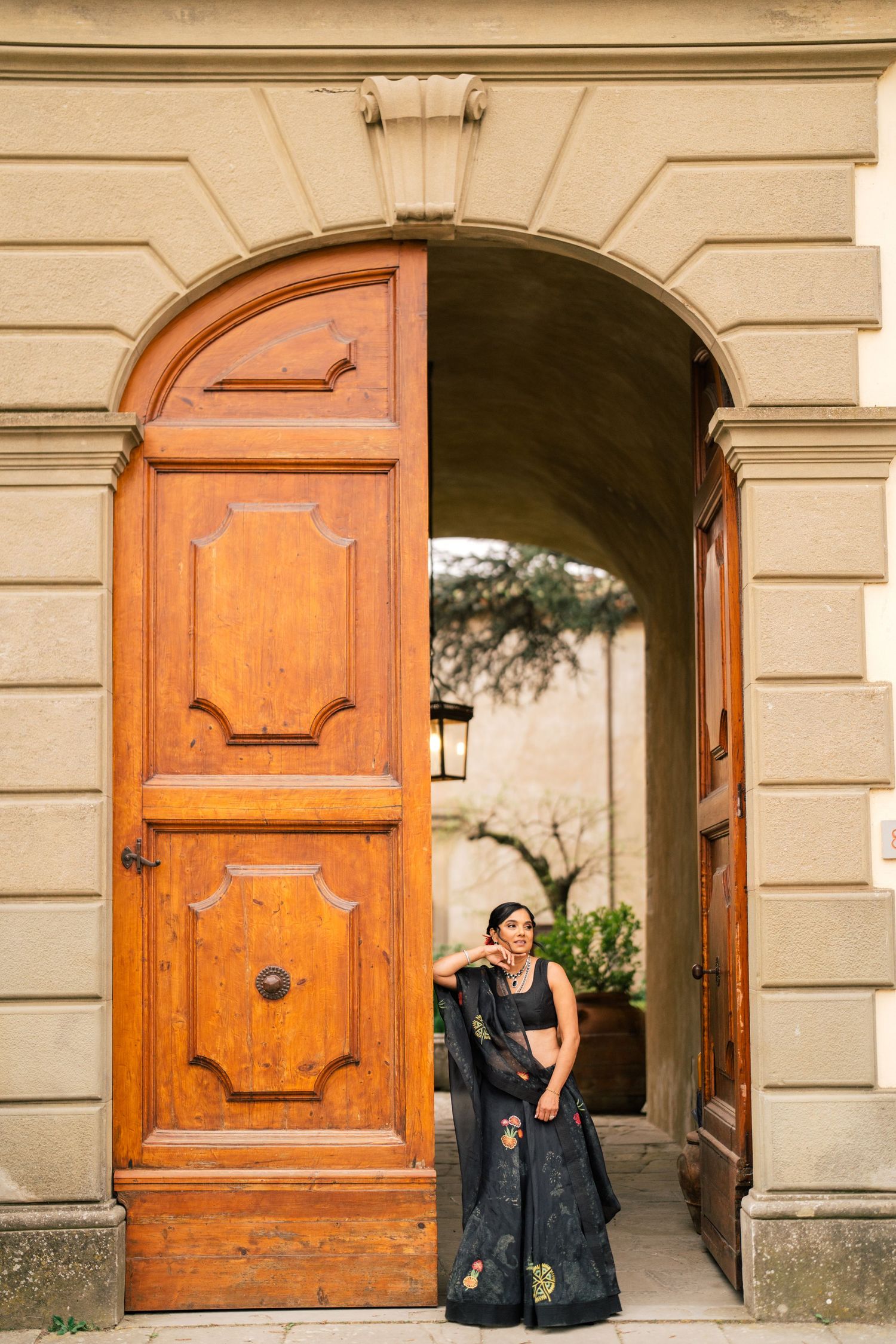 Couple in black formal wear standing in doorway of historic building with large wooden door.