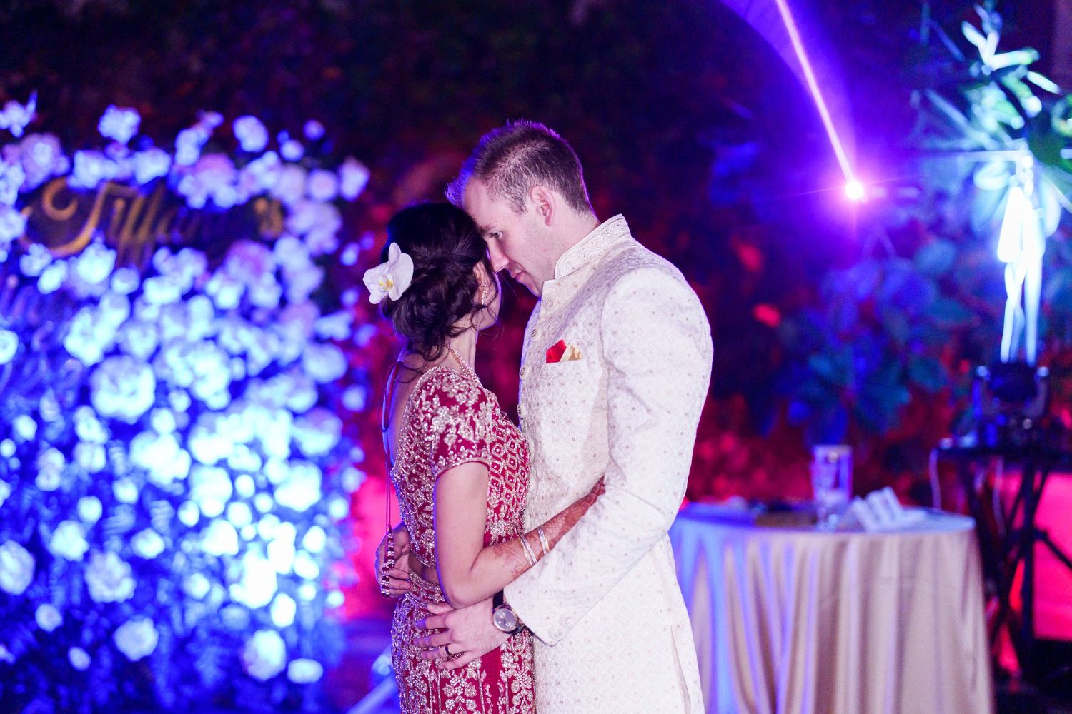 Romantic dance scene at an elegant reception with dramatic blue lighting and floral decorations.