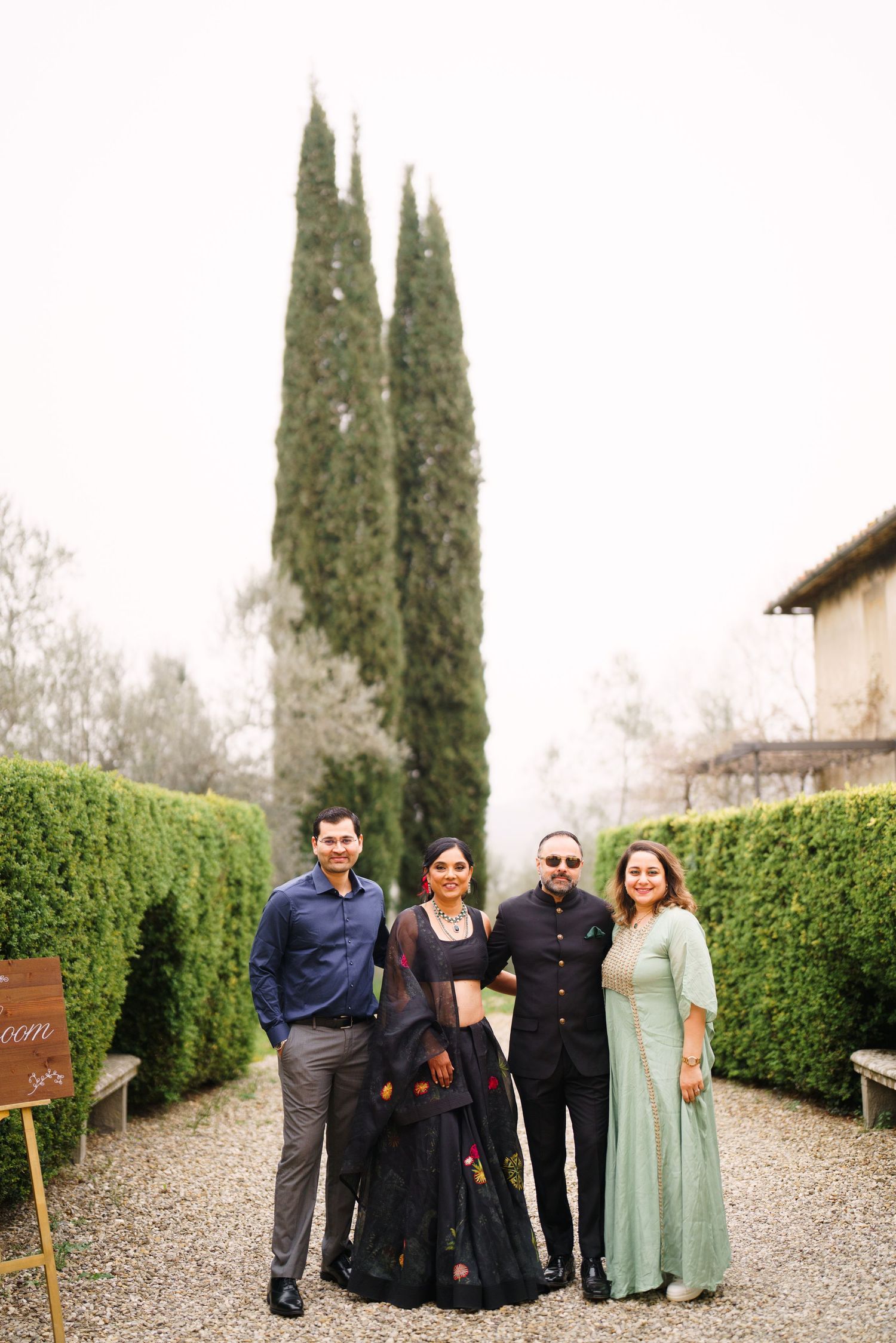 Friends and family gathered on a gravel walkway with Italian cypress trees in the background.