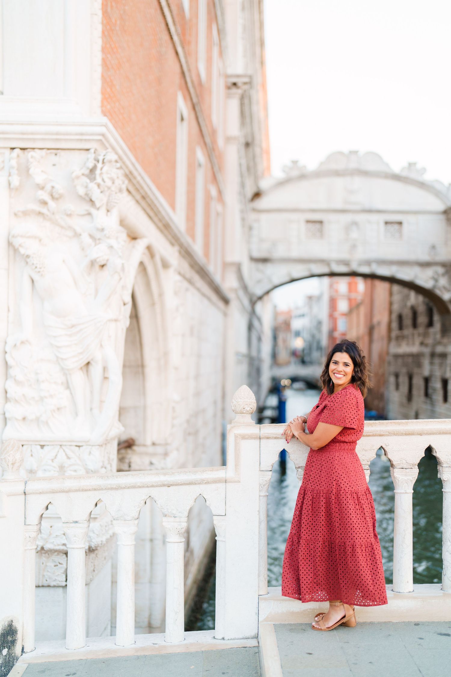 Woman in red dress posing near the Bridge of Sighs in Venice, Italy, with canal views.